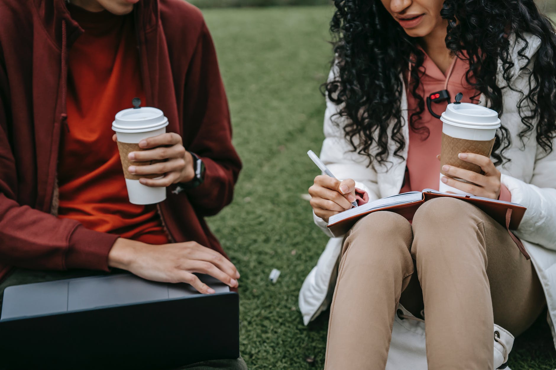 crop students with coffee studying on grassy lawn