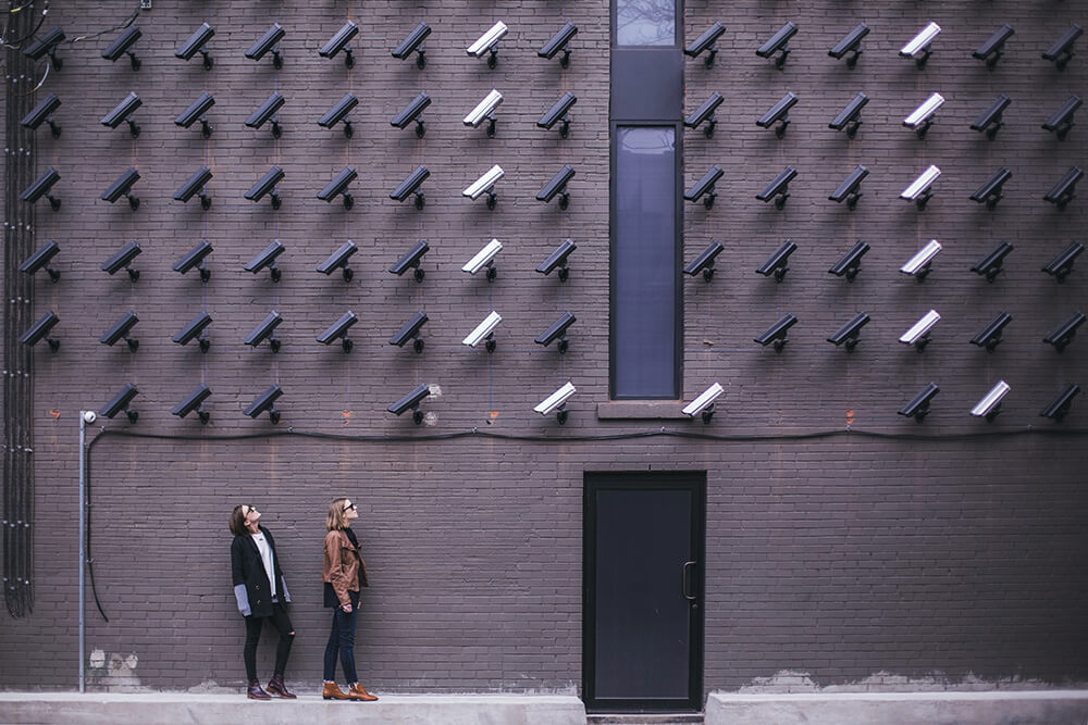 Two women facing security camera above mounted on structure.